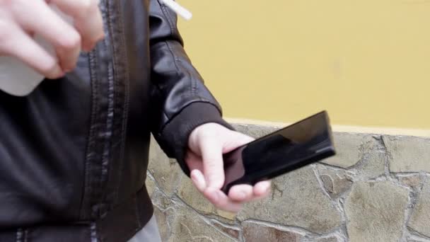 一个穿着皮夹克的男人用消毒剂喷雾擦拭手机表面 并在自然界中以抹布擦拭手机表面 大肠癌大流行期间的安全措施 — 图库视频影像