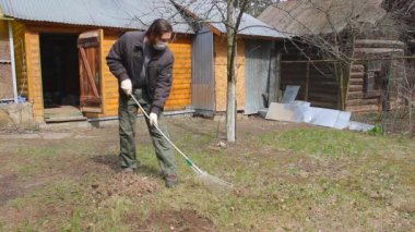 Koronavirüsten korunmak için tek kullanımlık maske takan genç adam, ağaç yapraklarından bahar temizliği yapıyor. Rüzgar saçlarını değiştiriyor. Doğa koruma kavramı ve çöpten orman temizliği kavramı.