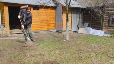 Koronavirüsten korunmak için tek kullanımlık maske takan genç adam, ağaç yapraklarından bahar temizliği yapıyor. Rüzgar saçlarını değiştiriyor. Doğa koruma kavramı ve çöpten orman temizliği kavramı.