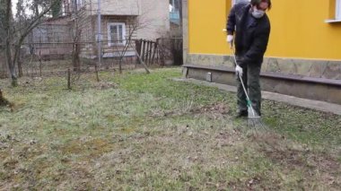 Koronavirüsten korunmak için tek kullanımlık maske takan genç adam, ağaç yapraklarından bahar temizliği yapıyor. Rüzgar saçlarını değiştiriyor. Doğa koruma kavramı ve çöpten orman temizliği kavramı.