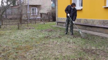 Koronavirüsten korunmak için tek kullanımlık maske takan genç adam, ağaç yapraklarından bahar temizliği yapıyor. Rüzgar saçlarını değiştiriyor. Doğa koruma kavramı ve çöpten orman temizliği kavramı.