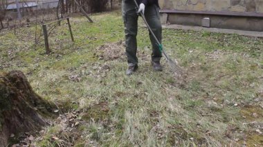 Koronavirüsten korunmak için tek kullanımlık maske takan genç adam, ağaç yapraklarından bahar temizliği yapıyor. Rüzgar saçlarını değiştiriyor. Doğa koruma kavramı ve çöpten orman temizliği kavramı.