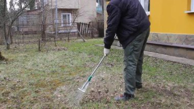 Koronavirüsten korunmak için tek kullanımlık maske takan genç adam, ağaç yapraklarından bahar temizliği yapıyor. Rüzgar saçlarını değiştiriyor. Doğa koruma kavramı ve çöpten orman temizliği kavramı.