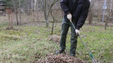 Koronavirüsten korunmak için tek kullanımlık maske takan genç adam, ağaç yapraklarından bahar temizliği yapıyor. Rüzgar saçlarını değiştiriyor. Doğa koruma kavramı ve çöpten orman temizliği kavramı.