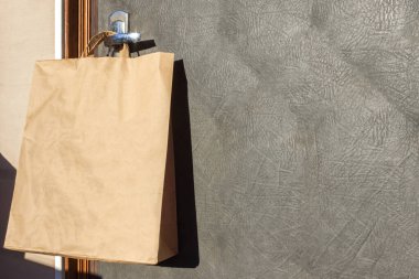 Kapı kolunda yiyecek asılı kağıt paketler. Koronavirüs salgını sırasında güvenli yiyecek teslimatı. Karantina zamanında dükkanlardan gelen hizmetler ve mahalle yardım kavramı