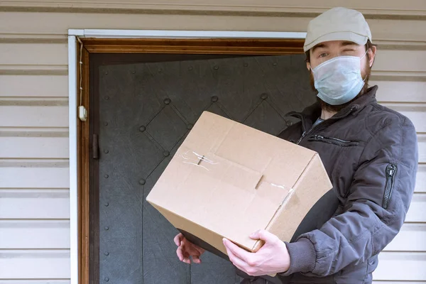 Courier in protective mask delivers parcel, Delivery service under quarantine, disease outbreak, coronavirus pandemic conditions. close-up of cardboard box holding by a male courier in a white cap