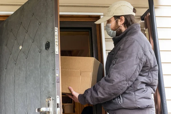 Courier in protective mask delivers parcel, Delivery service under quarantine, disease outbreak, coronavirus pandemic conditions. close-up of cardboard box holding by a male courier in a white cap