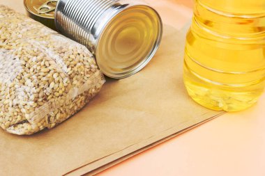 Pembe arka planda market yemeğinin olduğu kağıt torba. Coronavirus karantinası sırasında eve yiyecek teslimatı: konserve yiyecek, buğday, ayçiçeği yağı. Sağlıklı beslenme malzemeleri, gıda malzemeleri konsepti ve kopyalama alanı