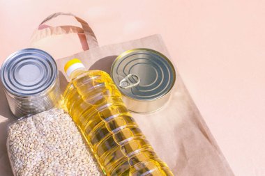 Pembe arka planda market yemeğinin olduğu kağıt torba. Coronavirus karantinası sırasında eve yiyecek teslimatı: konserve yiyecek, buğday, ayçiçeği yağı. Sağlıklı beslenme malzemeleri, gıda malzemeleri konsepti ve kopyalama alanı