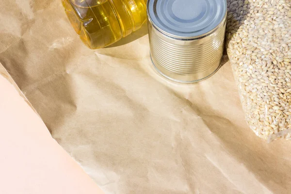 Paper bag with grocery food for hiking on pink background. Food delivery during coronavirus quarantine: canned food, grain cereals, oil. long storage food and products first necessity close-up