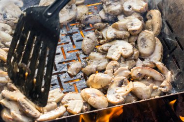 Sulu iştah açıcı şampiyonlar ızgarada ya da barbekü buharında pişiriliyor. Aşçı mantarları bir mutfak spatulasıyla karıştırır. Seçici odaklanma. Yemek arkaplanı. Vejetaryenler için lezzetli sağlıklı yemekler..