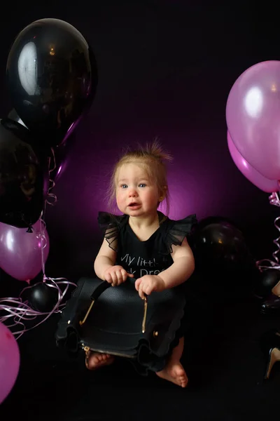 first year baby girl\'s birthday party day. ballons and holiday indoors. child\'s birthday. little pretty girl in her first black dress