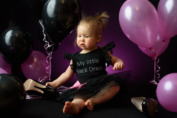 first year baby girl\'s birthday party day. ballons and holiday indoors. child\'s birthday. little pretty girl in her first black dress