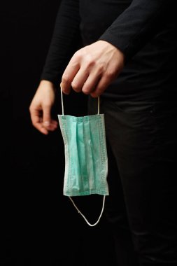 Siyah elbiseli bir adam elinde koruyucu bir maske tutuyor..