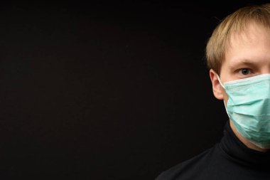 Tıbbi yüz maskesi olan orta yaşlı bir adam yakın plan karanlık arka planda pandemik koronavirüs hastalığını gösteriyor. Covid-19 salgın kirliliği kavramı.