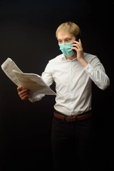 A young man in a medical mask quarrels on the phone analyzing the documents received. The concept of finding a solution to business problems due to the epidemic of coranavirus