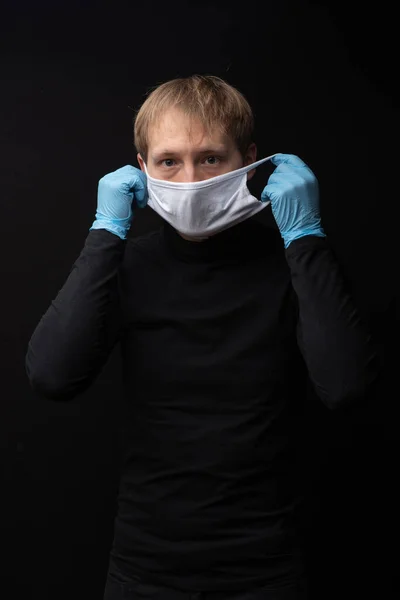 Man Black Clothes Black Background Medical Gloves Puts Medical Mask — Stock Photo, Image