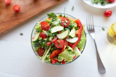 Domatesler, salatalık, marul ve kırmızı biberden yapılmış beyaz ahşap bir arka planda salata. Sağlıklı yeme kavramı.