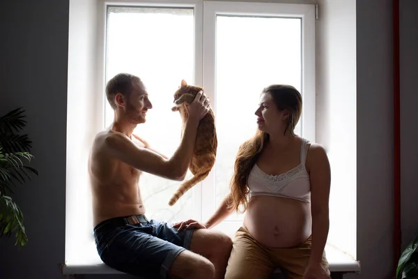 Birbirine Aşık Hamile Bir Çift Pencere Eşiğinde Oturup Kedileriyle Oynuyor — Stok fotoğraf