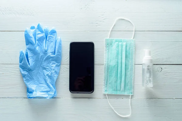 Medical gloves, phone, antiseptic and medical mask on a white wooden background.
