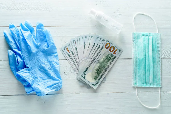 Medical gloves, money, antiseptic and medical mask on a white wooden background from above.