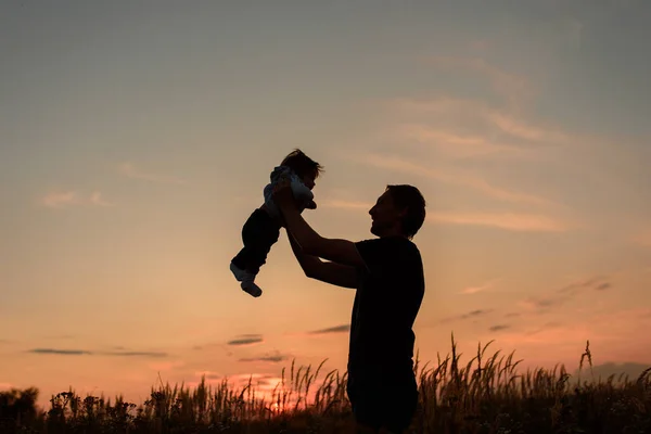 A father throws up his little daughter at sunset.