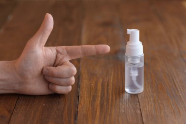 Erkek eli antiseptiğe işaret ediyor. Ahşap bir masa arkasında çekilmiş..