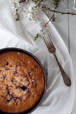 Beyaz ahşap arka planda vişneli turta. Yakınlarda eski bir gümüş kaşık ve bahar çiçekleri var..