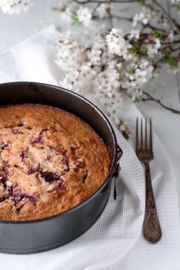 Beyaz ahşap arka planda vişneli turta. Yakınlarda eski bir gümüş kaşık ve bahar çiçekleri var..