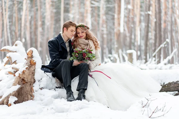 深爱着一束鲜花的年轻夫妇正坐在冬季森林的原木上 艺术品 冬天的婚礼复制空间 — 图库照片