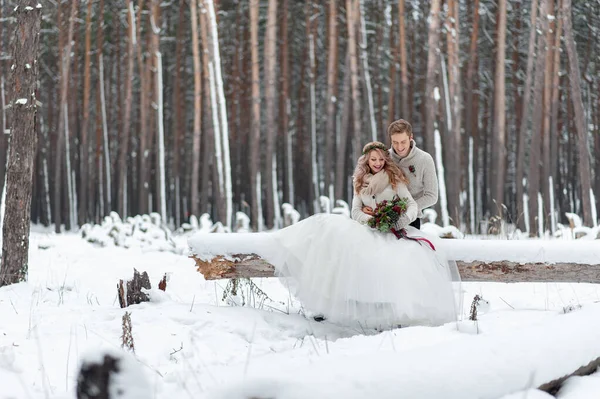深爱着一束鲜花的年轻夫妇正坐在冬季森林的原木上 艺术品 冬天的婚礼复制空间 — 图库照片