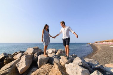 Genç ve güzel bir çift denizin arka planında yürüyor. Santorini Sahili 'nde çekilmiş..