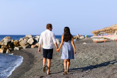 Genç ve güzel bir çift denizin arka planında yürüyor. Santorini Sahili 'nde çekilmiş..