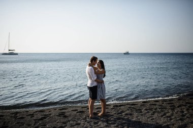 Santorini adasında denizin arka planında yürüyen genç bir çift.