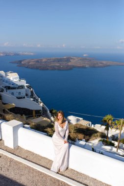 Thira, Santorini 'de Akdeniz' in arka planında poz veren beyaz elbiseli güzel gelin..