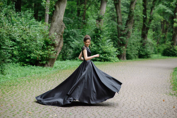 Young beautiful woman is spinning in a black dress in the park. The dress is beautifully developing.