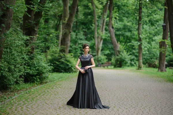 公園の黒いドレスを着た若い美しい女性 ハンドバッグを手に持って — ストック写真