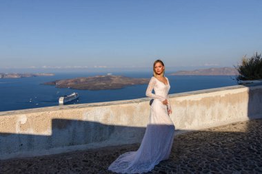 Thira, Santorini 'de Akdeniz' in arka planında poz veren beyaz elbiseli güzel gelin..