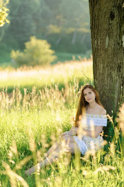 太陽の下で若い美しい少女の肖像画 日没の公園での夏の撮影会 日陰の木の下に女の子が座っている — ストック写真