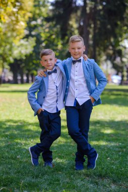 İki küçük çocuk, kardeşler takım elbise giymiş. Çocuklar parkta durup sarılıyorlar..