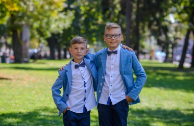 İki küçük çocuk, kardeşler takım elbise giymiş. Çocuklar parkta durup sarılıyorlar..