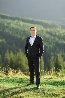 Gün batımında dağların arka planında yalnız bir damadın portresi..