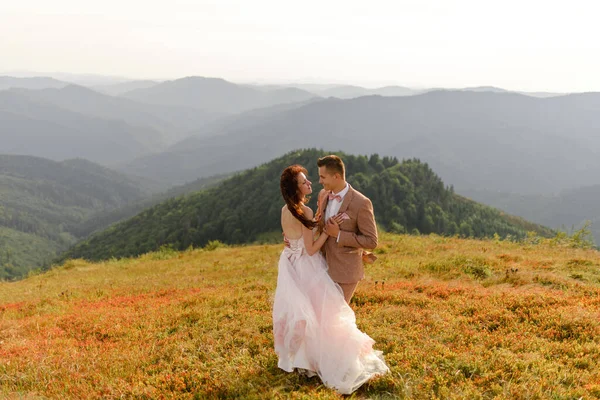 新娘和新郎相邻而去 日落了秋山背景下的婚纱照 大风吹得头发和衣服都鼓起来了 — 图库照片