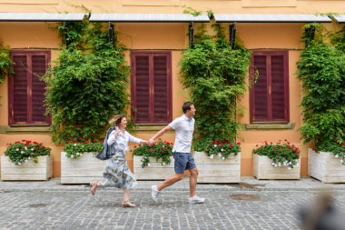 Sevgili çift kol kola koşuyor çerçevede.