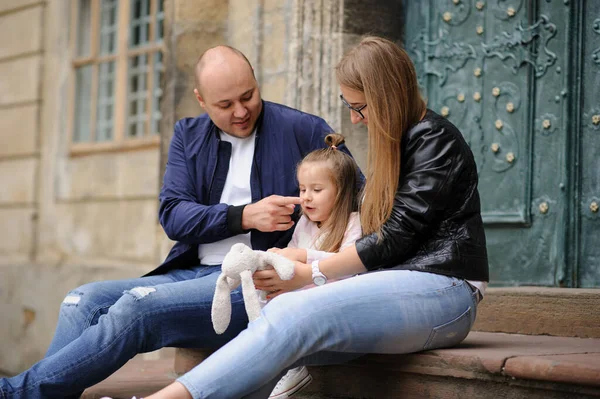 Parents and their daughter are sitting on the steps of an old church.