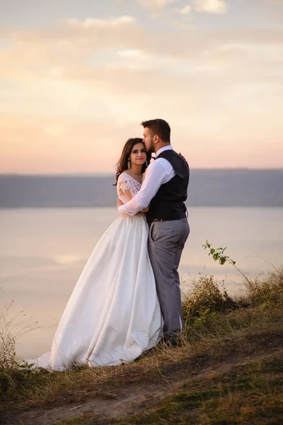 日落时 新娘和新郎在湖畔拥抱 — 图库照片