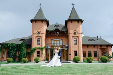 Gelin ve damat, şatoya benzeyen bir restoranın arka planında sarılıyorlar..