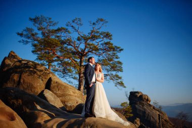 Gelin ve damat bir uçurumun üstünde duruyorlar. Gün batımı.