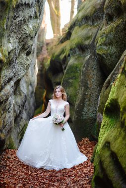 Güzel gelin sarışını Dar bir vadide bir buket çiçekle duruyor.