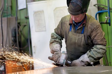 Metal endüstrisi: fabrika kaynakçısı atölyede aşındırıcı diskle çelik levha öğütüyor